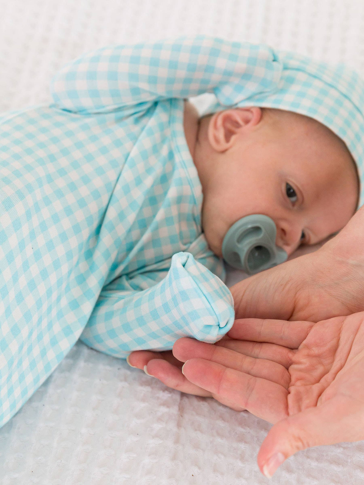 Newborn baby wrapped in a blue checkered swaddle with a pacifier, held by an adult hand.