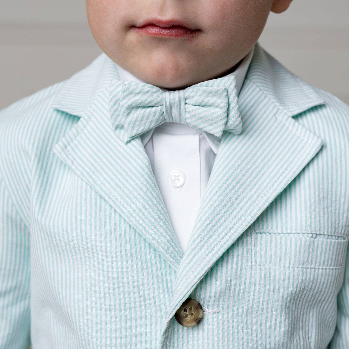Child wearing a mint striped suit with a bow tie against a neutral background