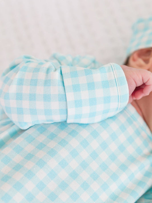 Close-up of a baby's arm in a blue and white checkered outfit against a neutral background