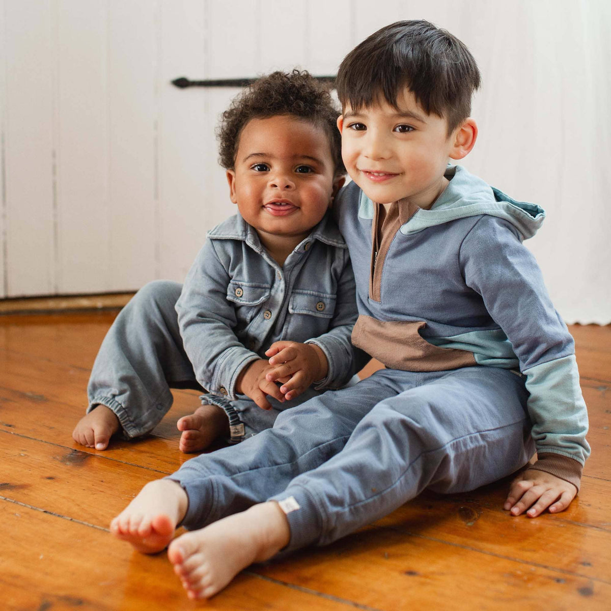 Two children sitting on a wooden floor wearing matching blue outfits.