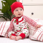 Baby in red and white striped outfit with holiday pattern, sitting on a plaid blanket.