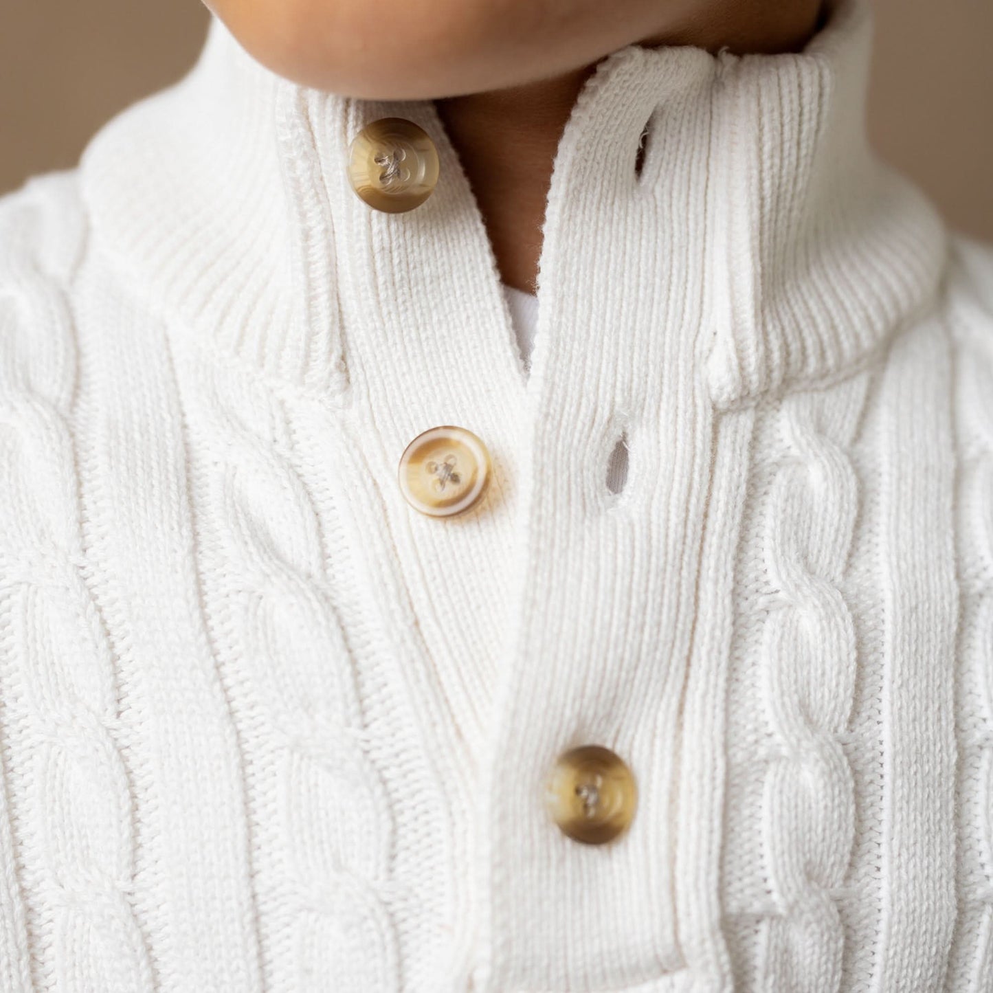 Close-up of a white cable-knit cardigan with button details on a neutral background