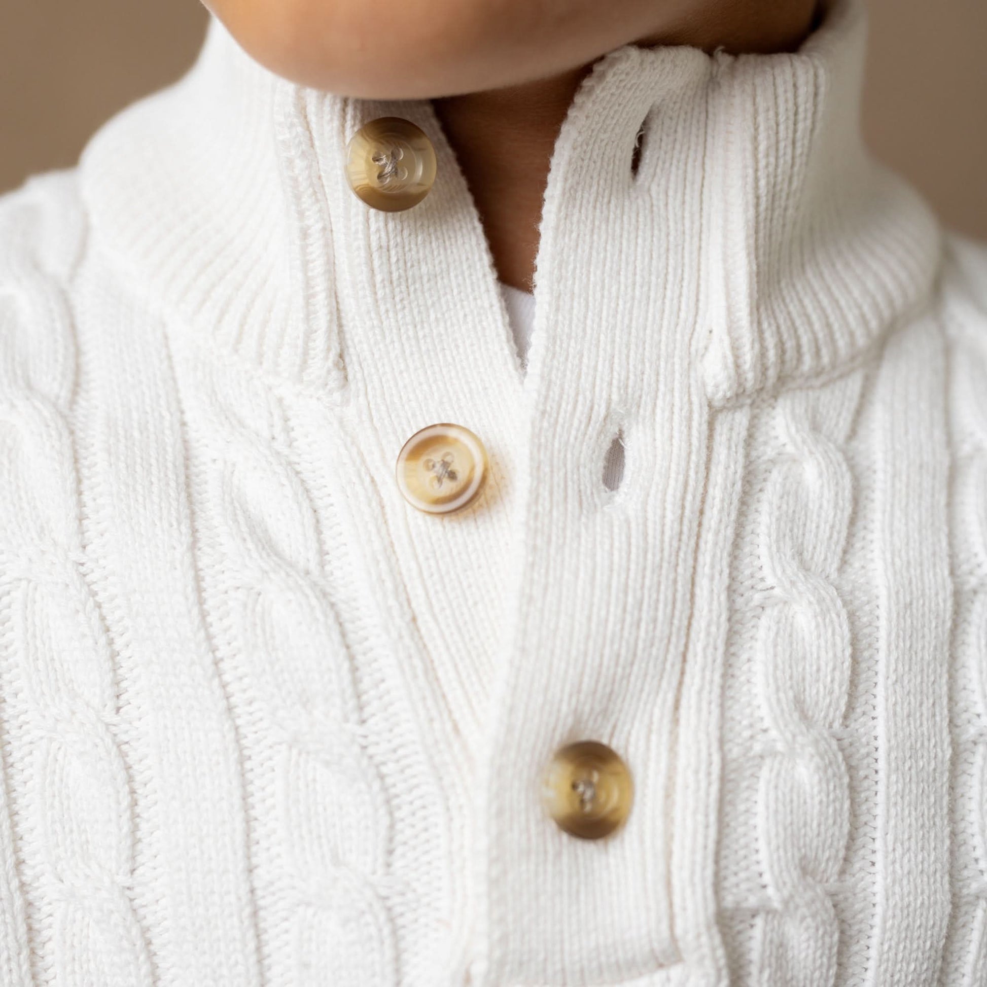 Close-up of a white cable-knit cardigan with button details on a neutral background