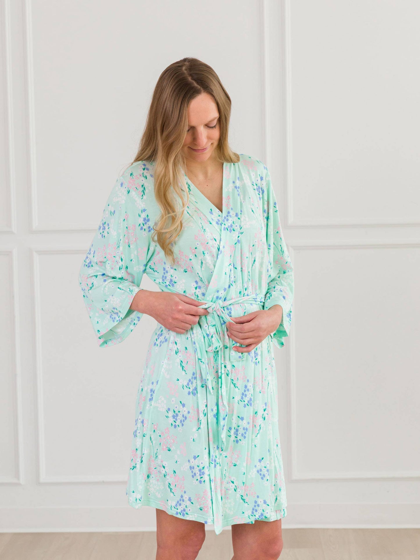 Woman wearing a light green floral robe against a white paneled wall.