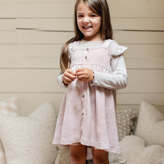 Young girl wearing a light pink dress with ruffled sleeves, standing against a neutral background.