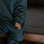 child wearing a dark green jogger set with a button.