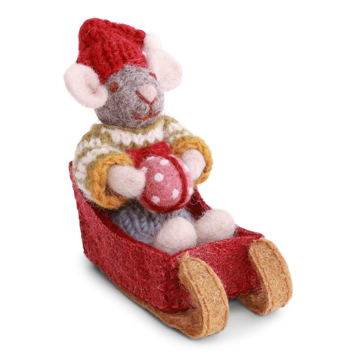 A handmade felt mouse doll wearing a red knit hat and a cream, yellow, and brown knit sweater, sitting in a red felt sleigh and holding a red ornament with white polka dots, set against a plain white background.