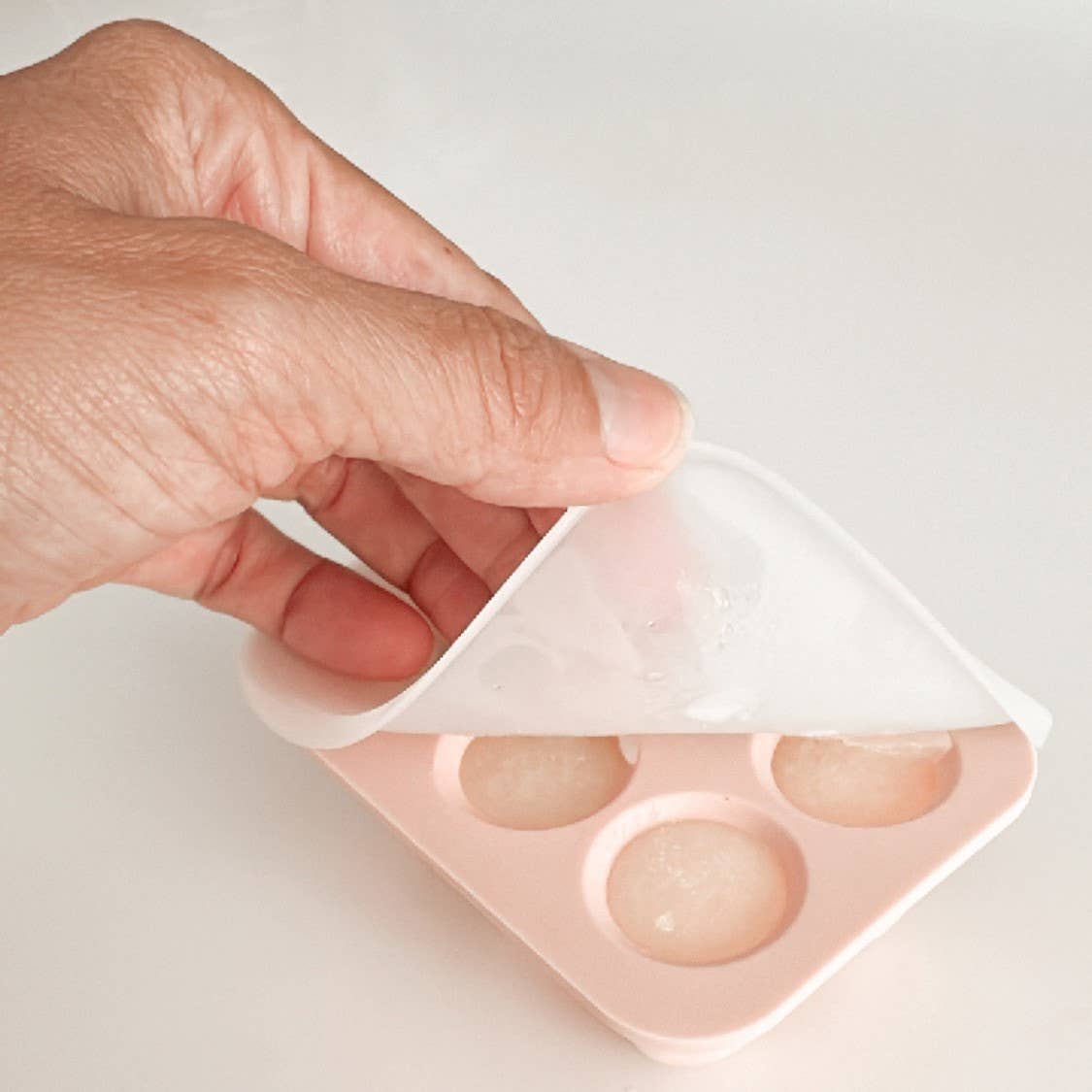 Hand holding a pink silicone mold with circular cavities on a light background
