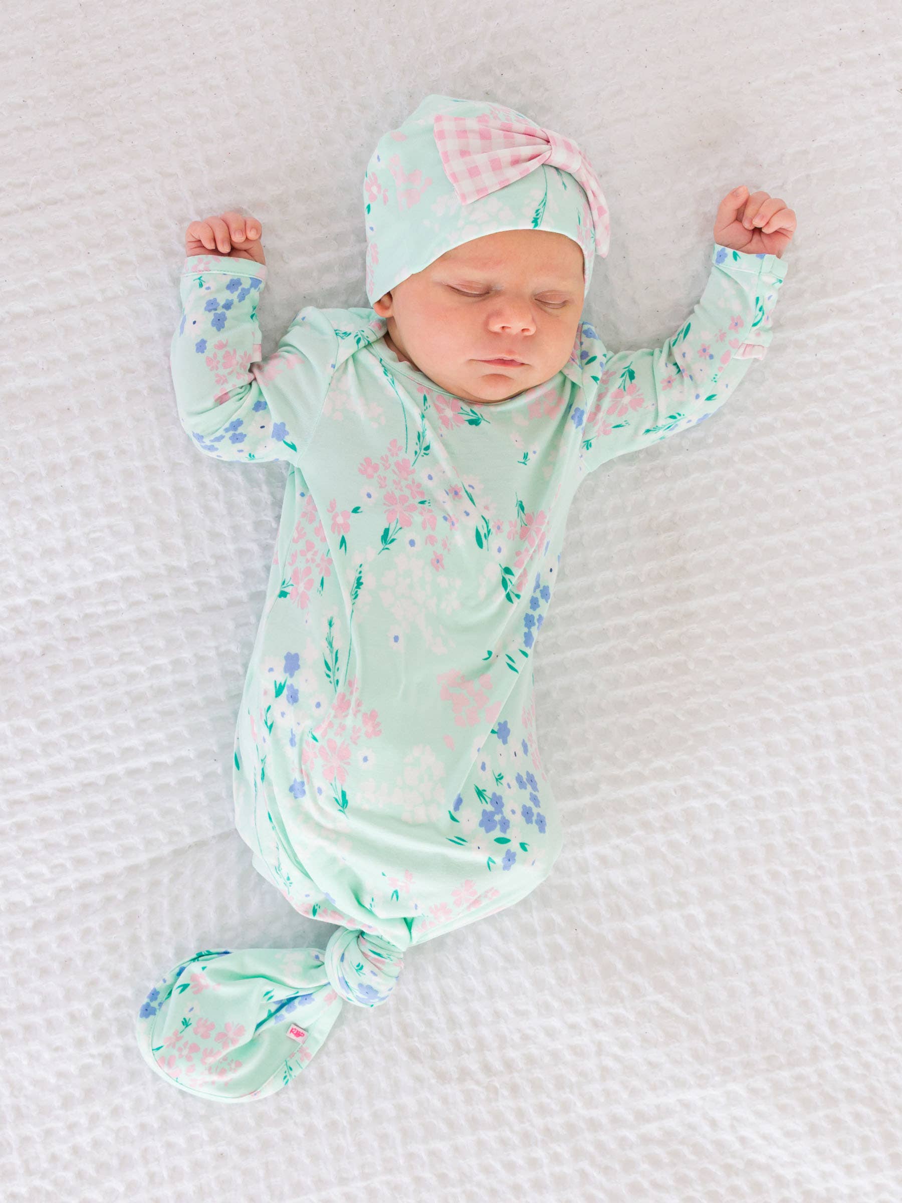 Newborn baby in a floral outfit and hat on a textured white blanket