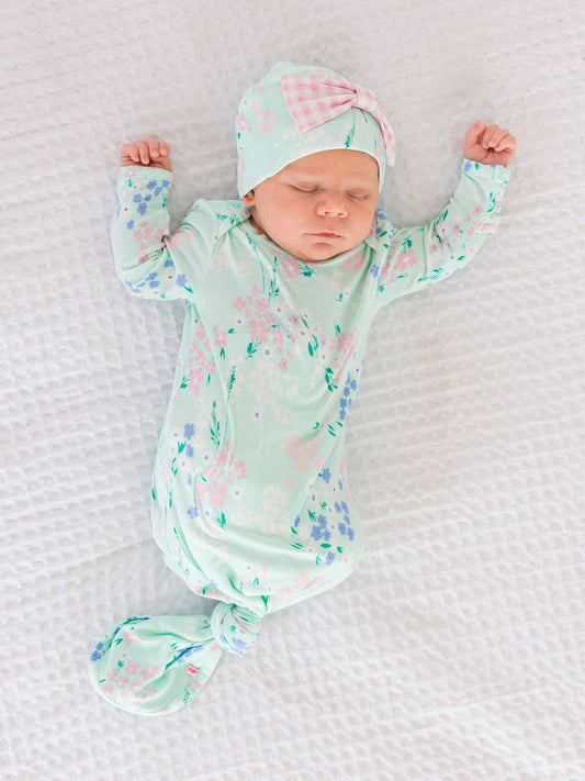 Newborn baby in a floral outfit and hat on a textured white blanket