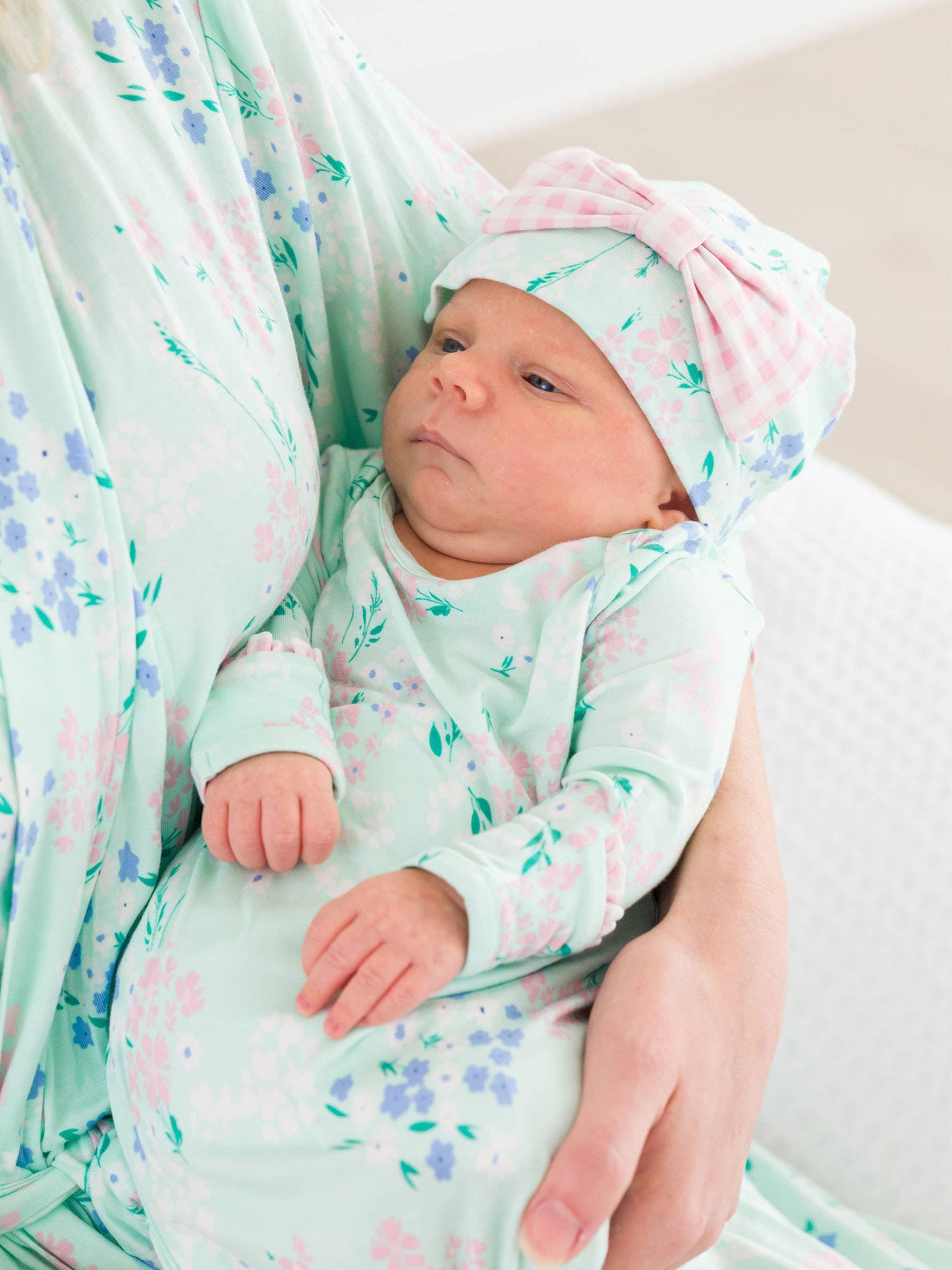 Newborn baby in a floral outfit and hat being held by a person in a matching robe.