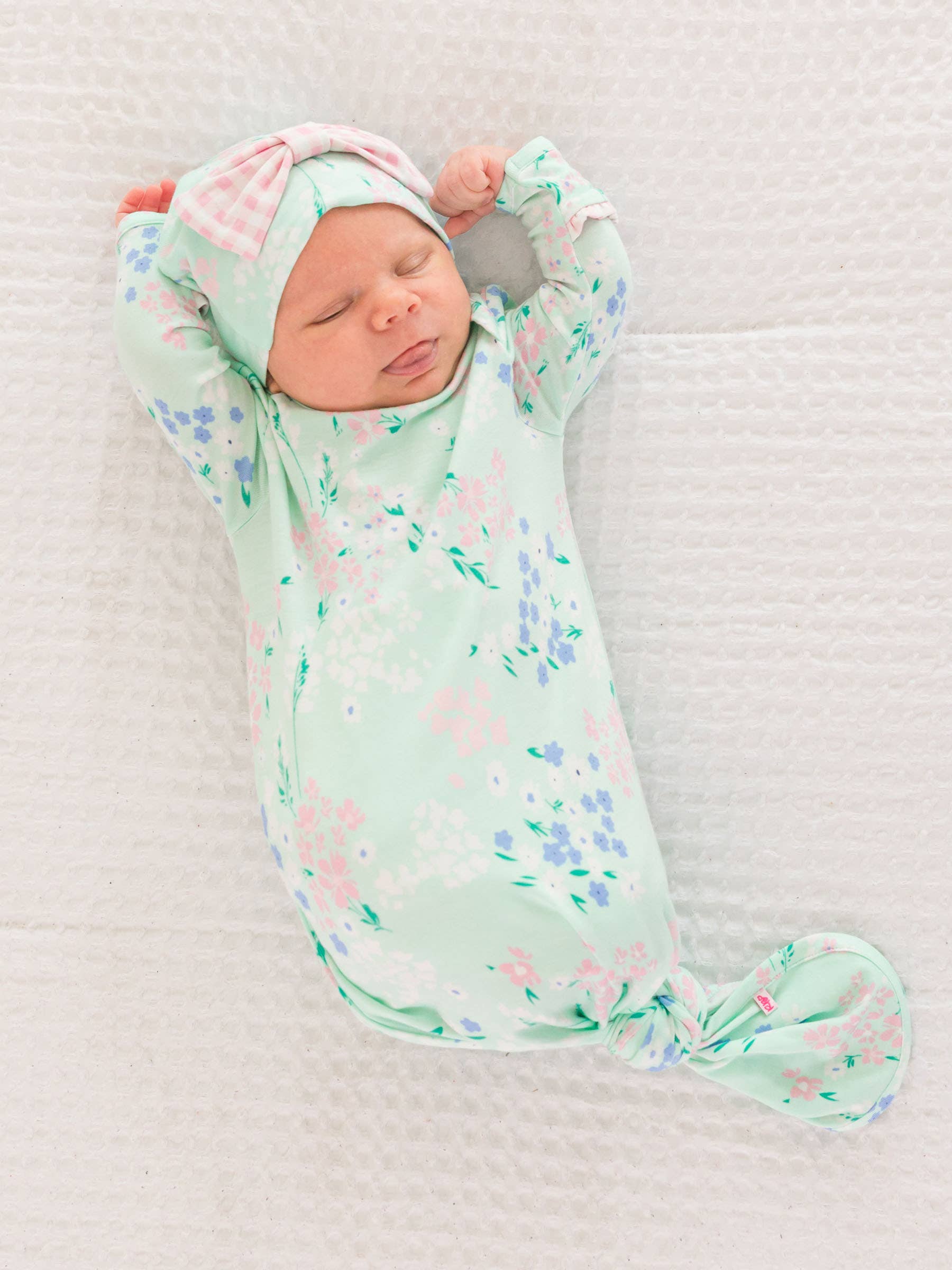 Newborn baby wrapped in a floral knotted gown with matching hat on a white blanket