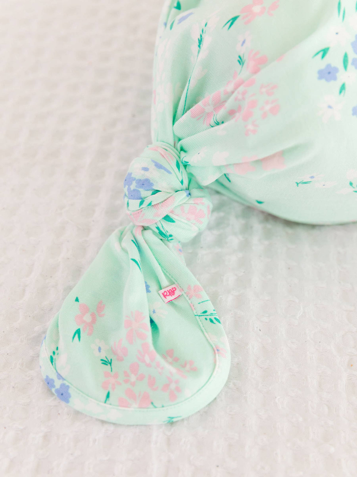 Mint green knotted baby gown with floral pattern on a light pink background
