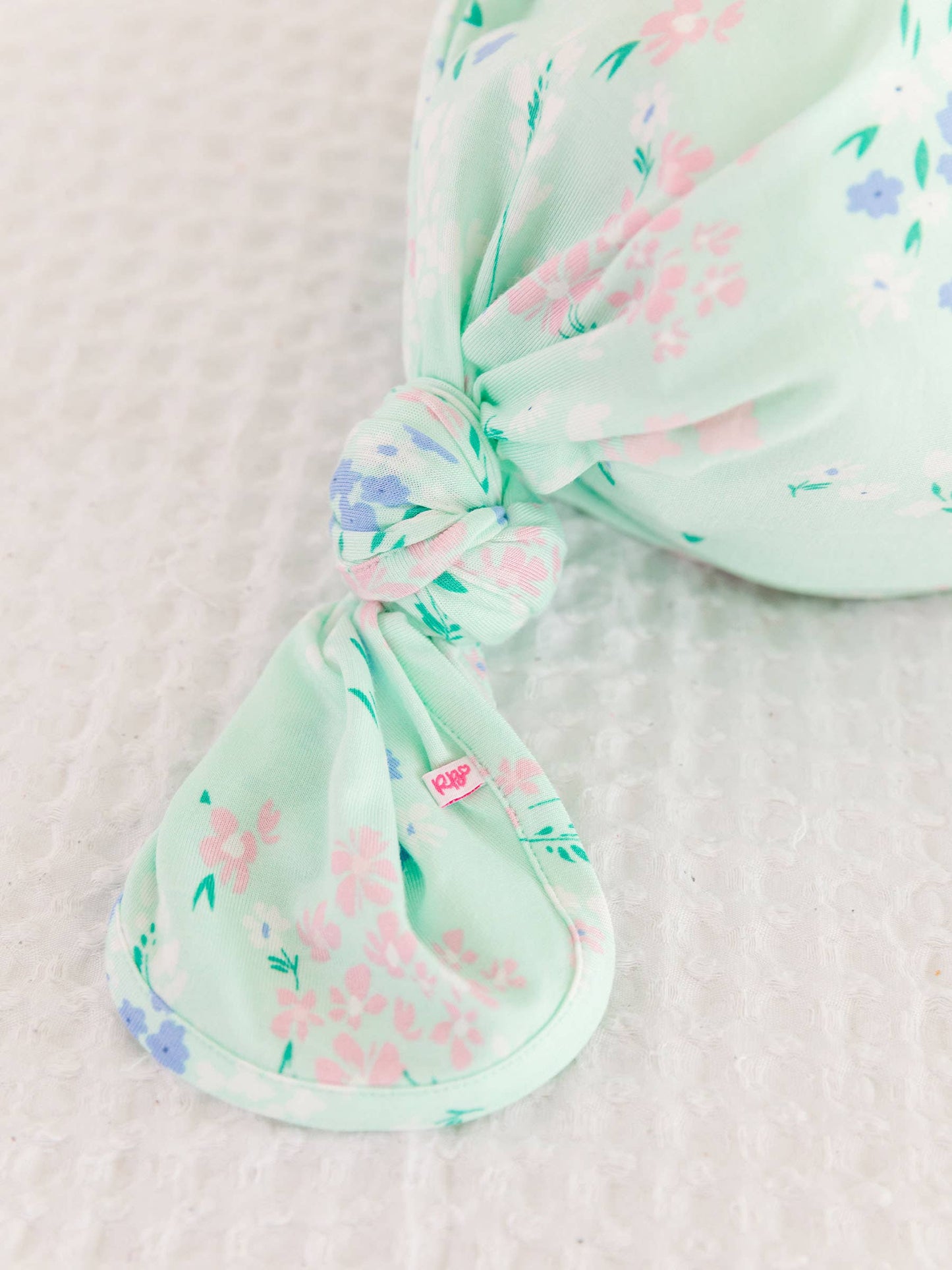 Mint green knotted baby gown with floral pattern on a light pink background