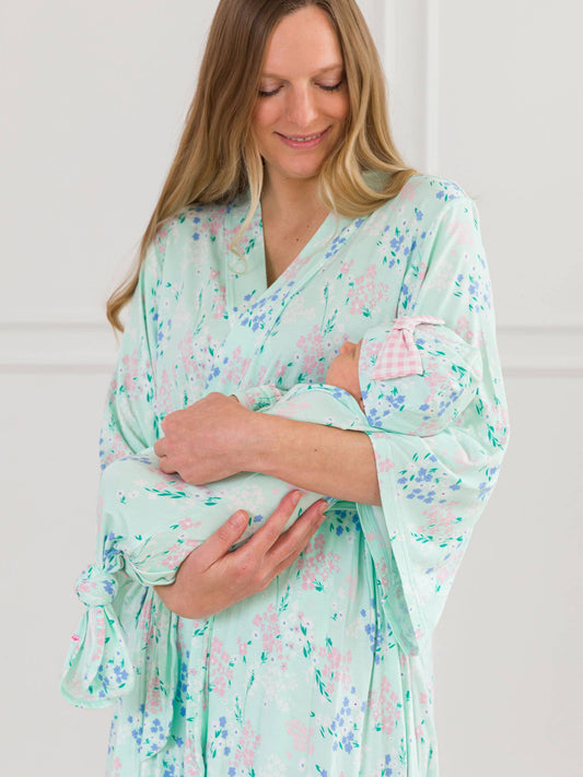 Woman in a floral robe holding a baby against a white background