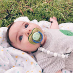 Baby lying on grass with a pacifier attached to pacifier clip