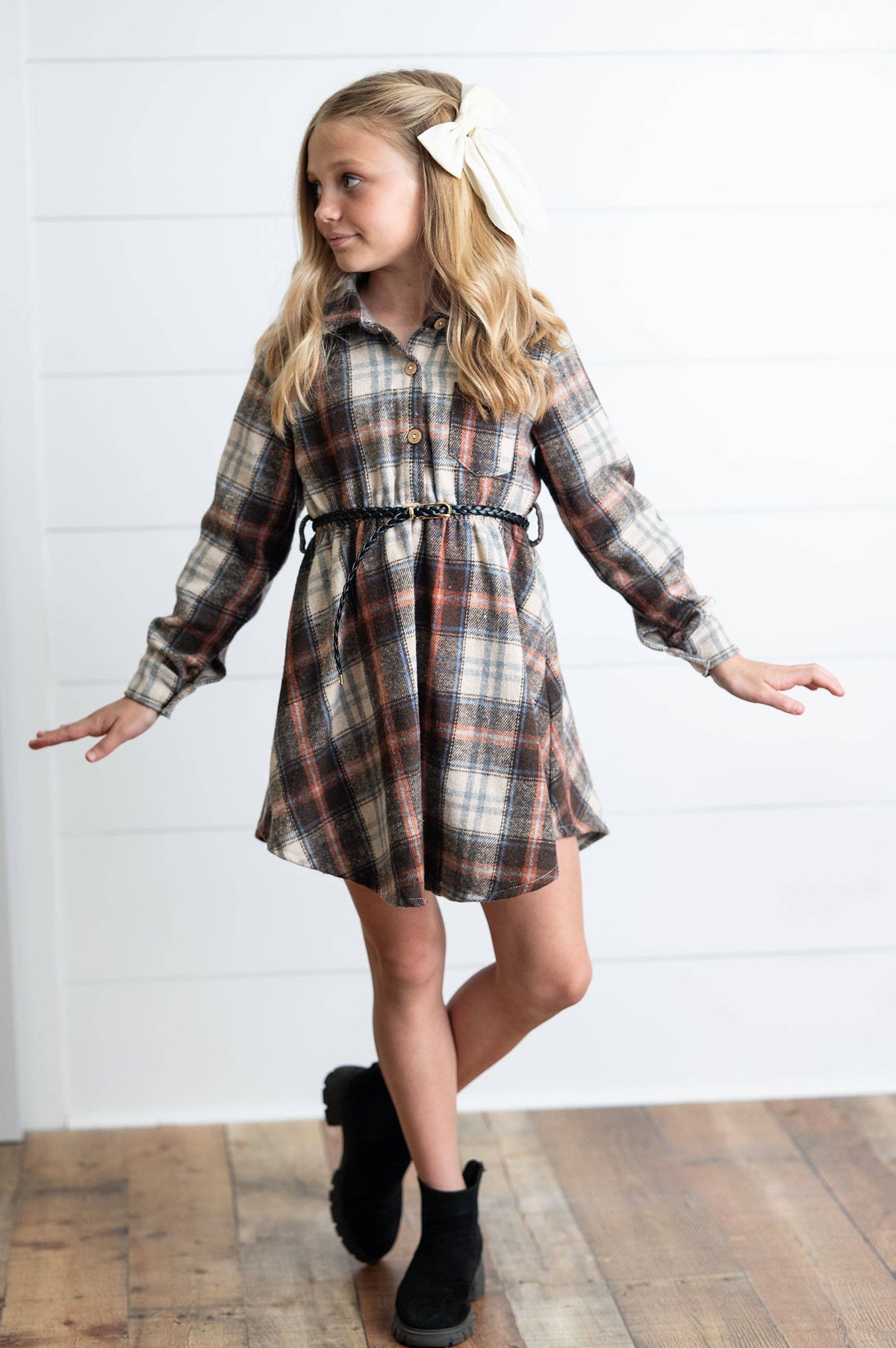 Young girl wearing a plaid dress with a belt and black boots on a white background