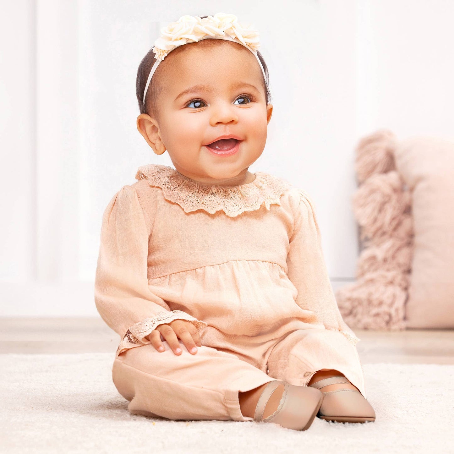 baby girl wearing a stylish special occasion beige baby girl romper and a flowered headband against a white background
