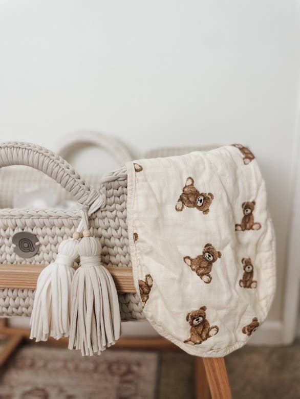 Baby burp cloth with teddy bear pattern draped over a woven basket on a wooden surface.