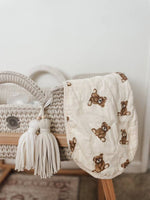 Baby burp cloth with teddy bear pattern draped over a woven basket on a wooden surface.