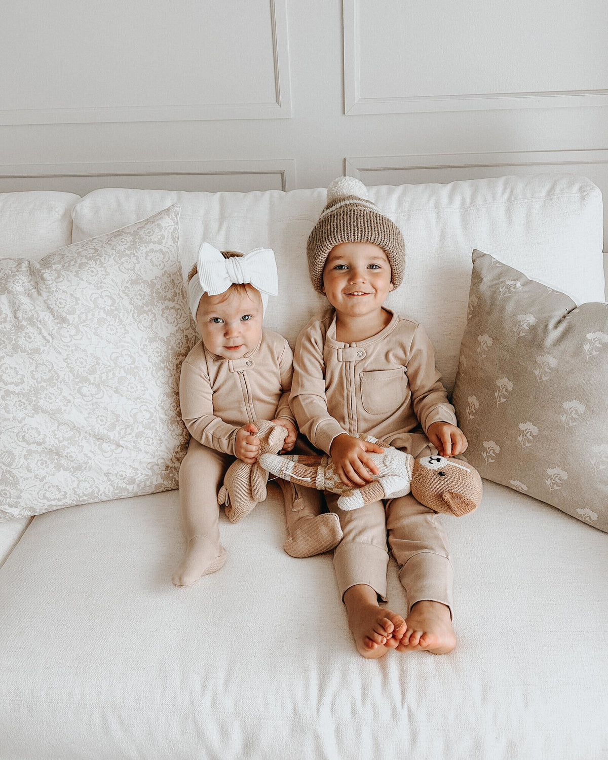 Two children in matching outfits sitting on a couch with pillows.